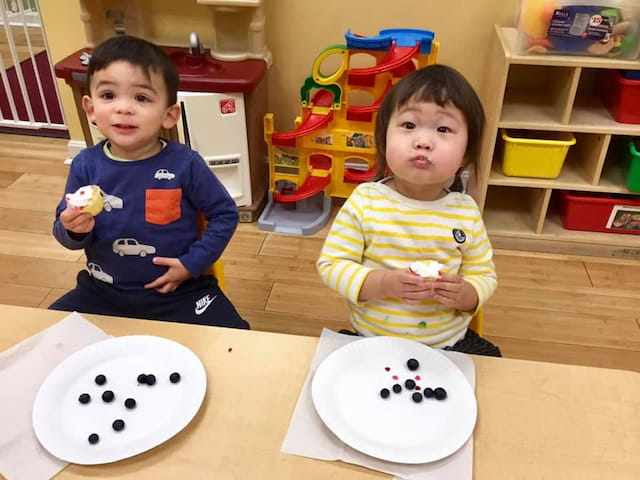 a couple of kids sitting at a table with a plate of food