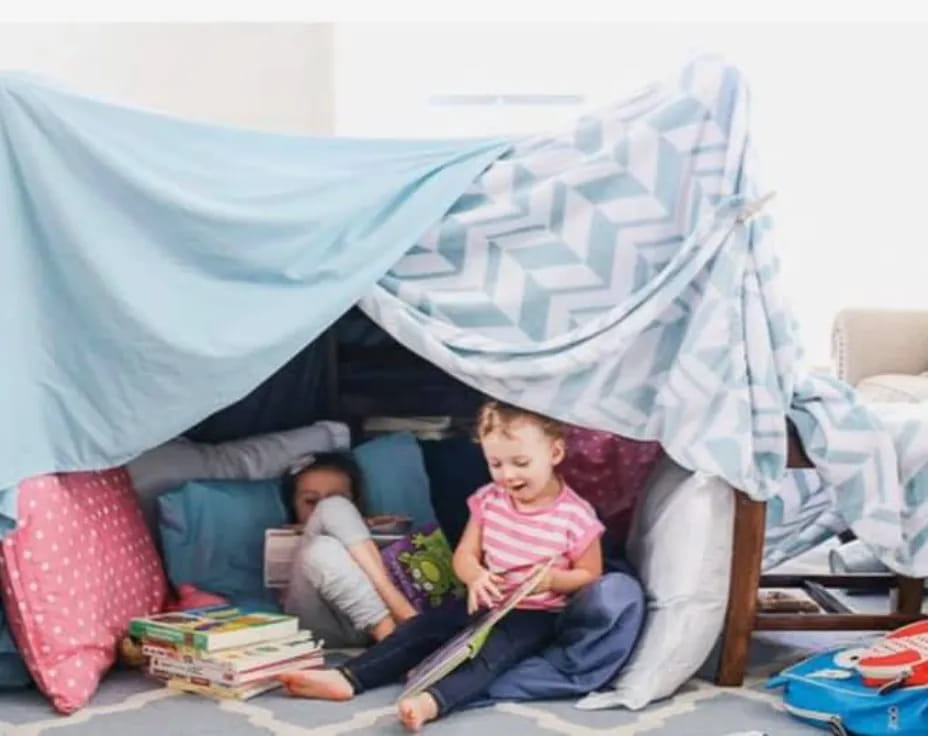 a couple of children sitting on a couch with a blue tent behind them