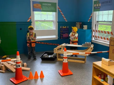 a couple of kids in a room with construction cones and a bench
