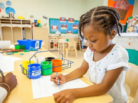 a child sitting at a table writing on paper