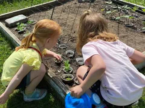 two girls planting plants in a garden