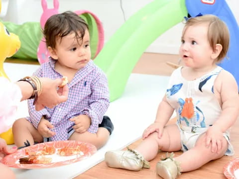 a couple of young girls sitting on the floor eating cake