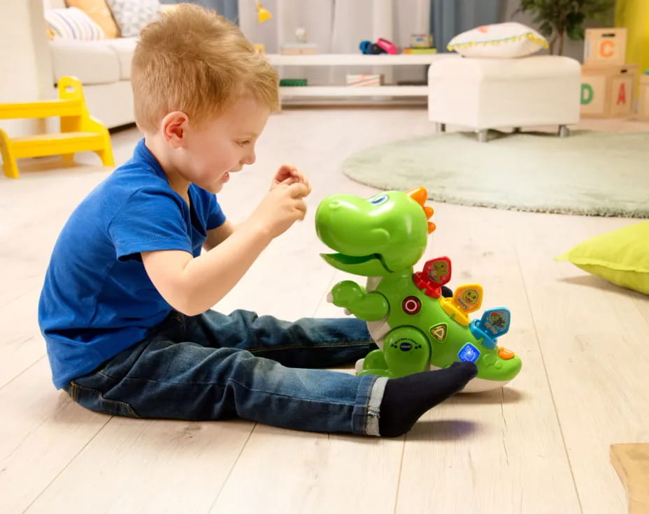a boy sitting on the floor next to a toy dinosaur