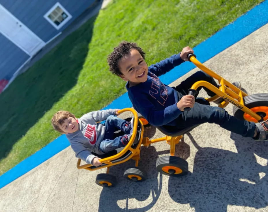 a couple of boys playing on a toy tricycle
