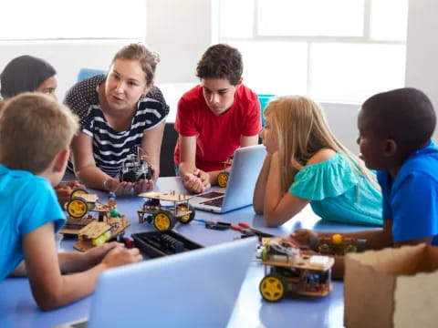 a group of kids sitting around a table with a laptop