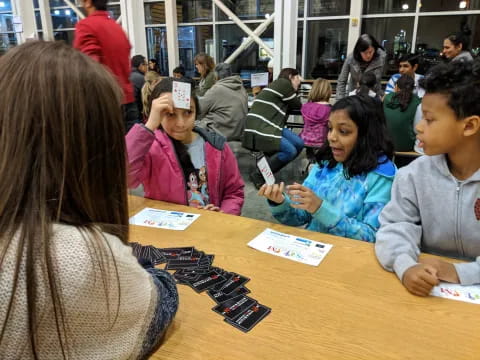 a group of children sitting at a table playing cards