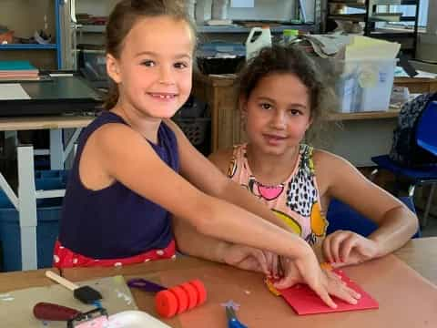 a couple of girls sitting at a table with tools