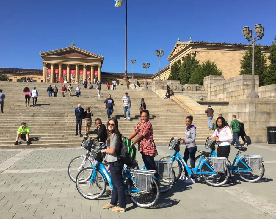 a group of people with bicycles in a courtyard with a building in the background