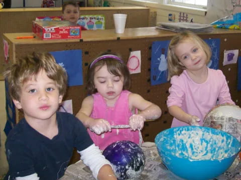 a group of children sitting in a room with a bowl and a shelf