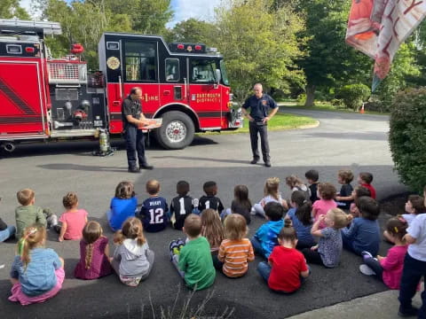 a group of people sitting on the ground watching a firetruck