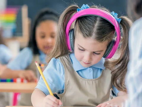 a young girl wearing headphones and writing on a book