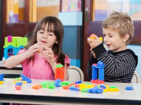 a boy and girl sitting at a table with toys