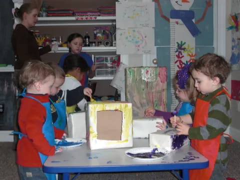 a group of kids stand around a table with a cake