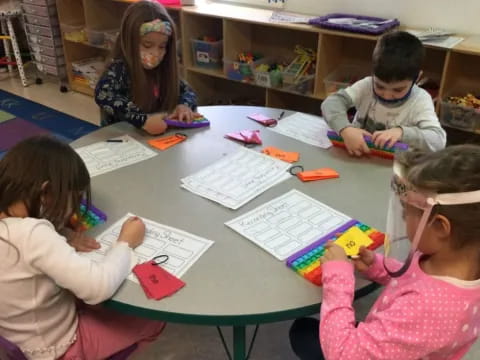 a group of children sitting at a table with paper and pencils