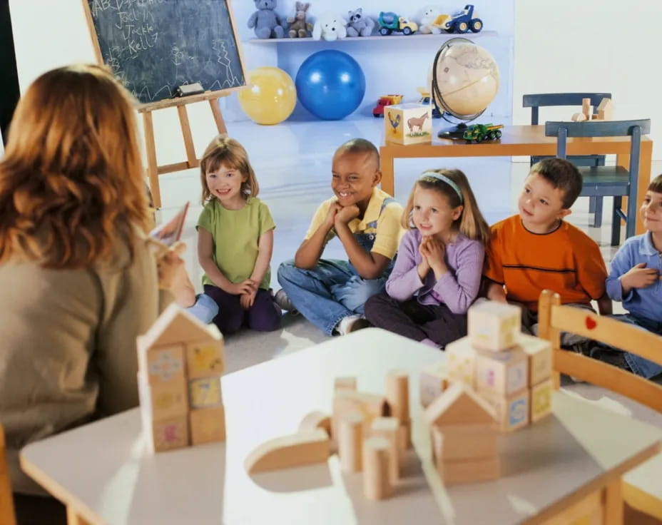 a group of children sitting around a table with a woman and a man