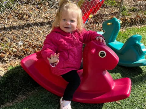 a child in a pink coat on a red toy in a yard