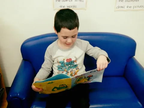 a boy sitting on a blue couch reading a book