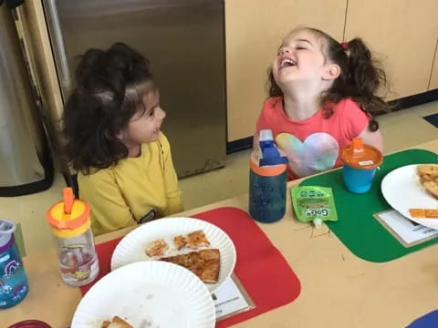a couple of girls sitting at a table with food on it