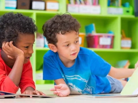 a couple of children sitting at a table looking at a book