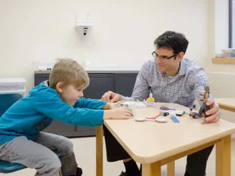 a person and a boy sitting at a table with a game controller