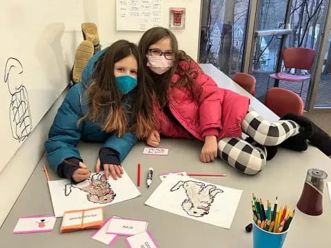 a couple of girls sitting at a table with a drawing