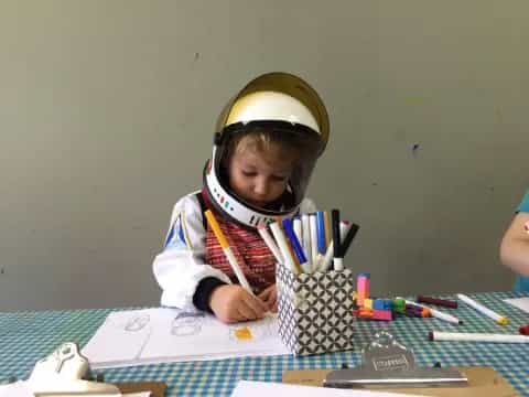 a young girl wearing a helmet and goggles and writing on a piece of paper
