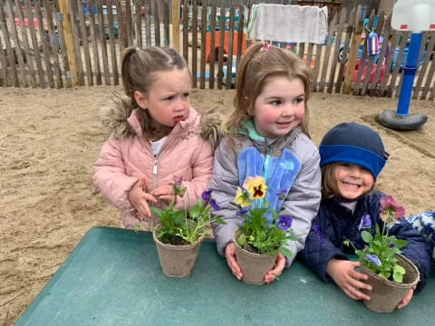 a group of children sitting on a table with plants in pots
