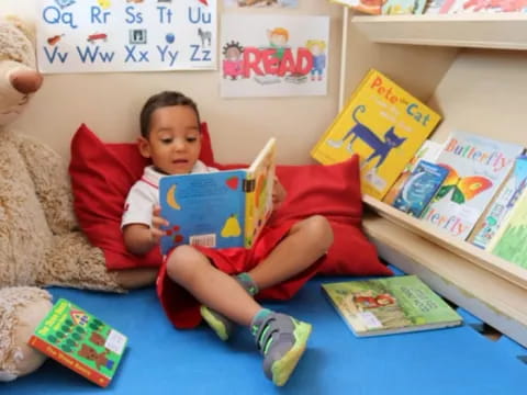 a boy sitting on a bed with books and a stuffed bear