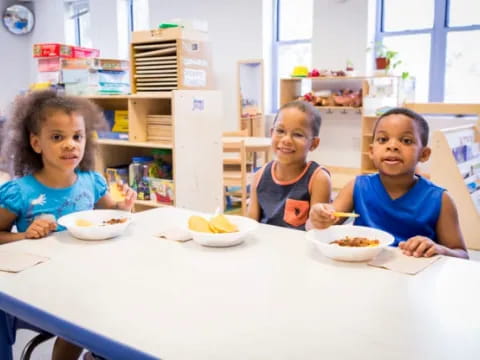 a group of children sitting at a table with food
