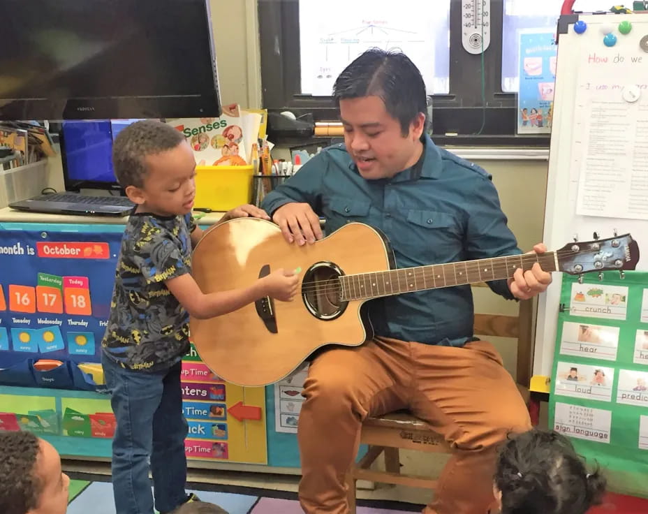 a person playing a guitar with a boy watching