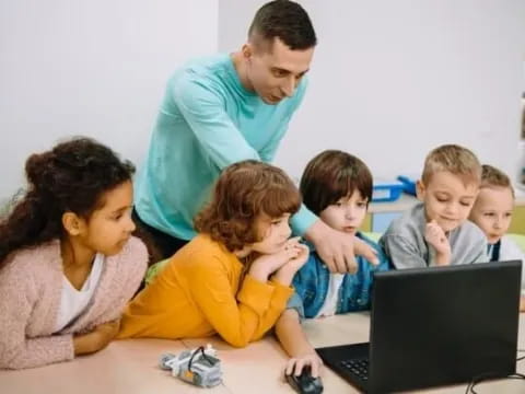 a person and a group of children looking at a laptop