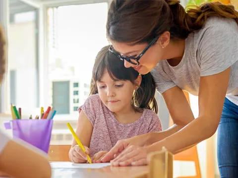 a woman helping a child with a pencil