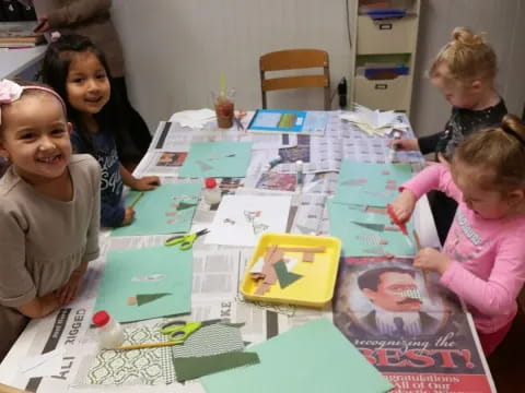 a group of children sitting around a table with colorful paper on it