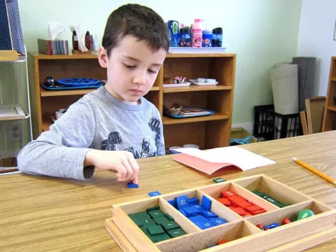 a boy sitting at a table with a book and pencils