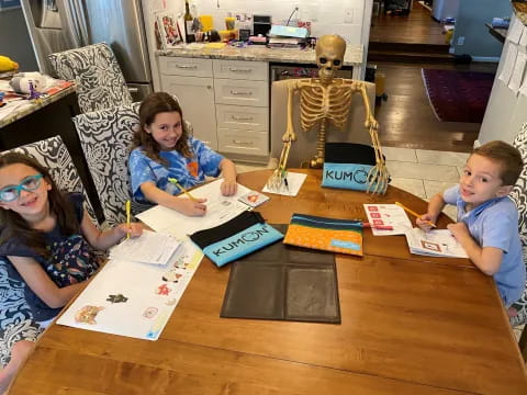 a group of children sitting at a table with books and drawings on it
