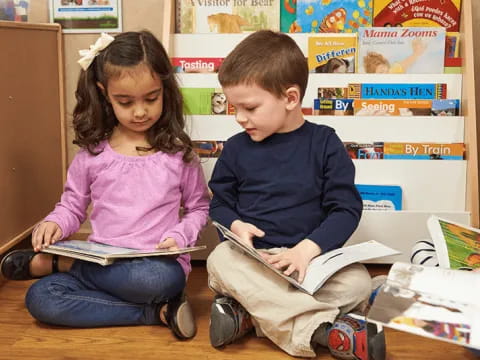 a boy and girl sitting on the floor reading a book