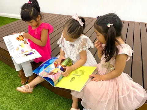a group of girls sitting on a bench reading a book