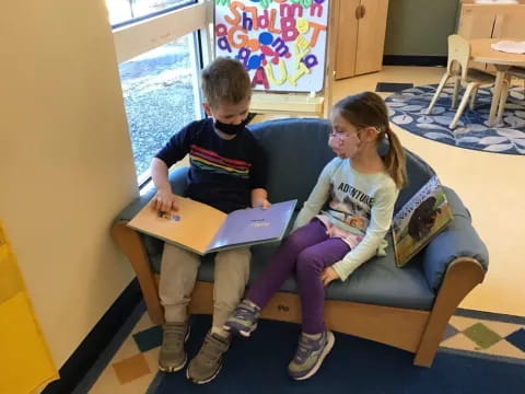 a boy and girl sitting on a couch looking at a laptop