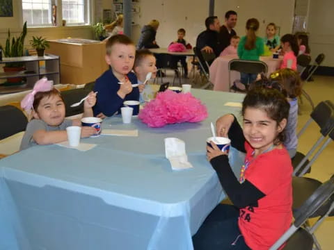 a group of children sitting at a table with cups and a cake
