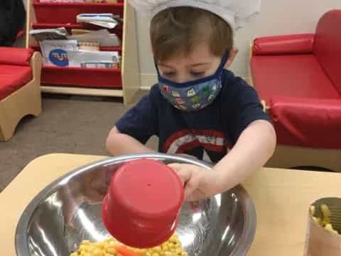 a child in a white hat and blue shirt eating a bowl of food
