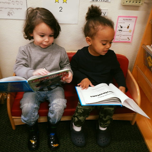 a couple of children sitting on a bench reading books