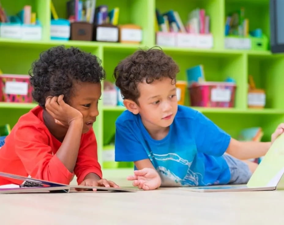 a couple of young boys sitting at a table in a library