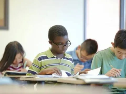 a group of children sitting at a table writing on paper