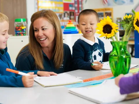 a person and children sitting at a table with a vase of sunflowers