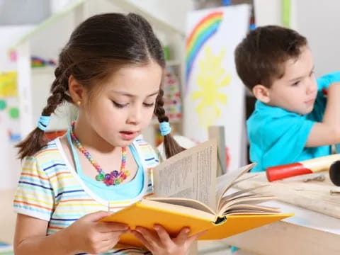 a young girl reading a book to a young boy