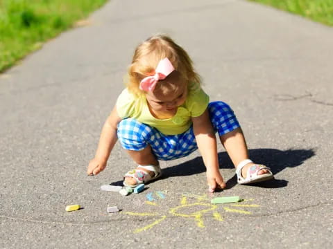 a little girl playing with chalk on the sidewalk
