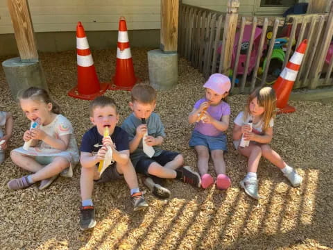 a group of kids sitting on the ground eating ice cream cones