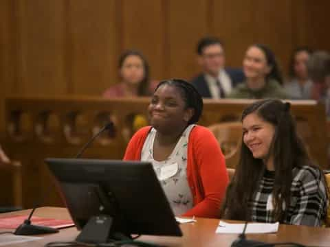 a woman and a man sitting at a desk with a laptop