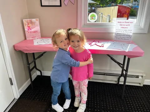 two children standing in front of a pink table