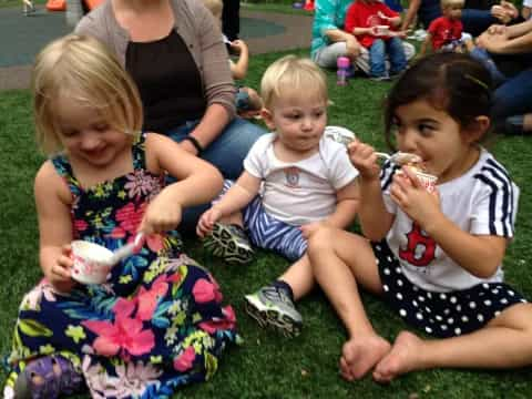 a group of children sitting on the grass eating ice cream